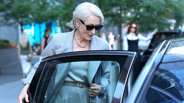 A sharply dressed older woman ducks into a car.