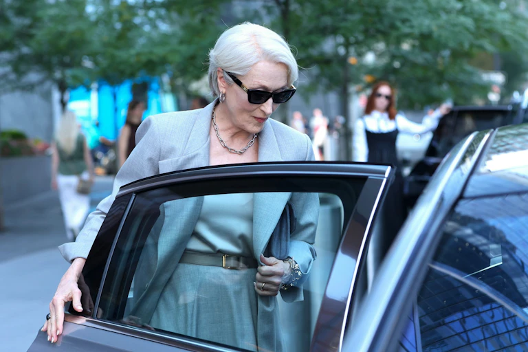 A sharply dressed older woman ducks into a car.