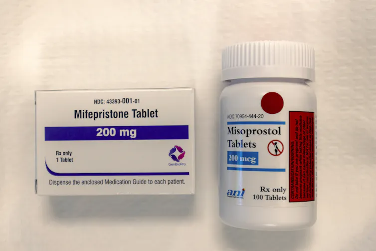 A packet of mifepristone and a pill bottle of misoprostol on a white background
