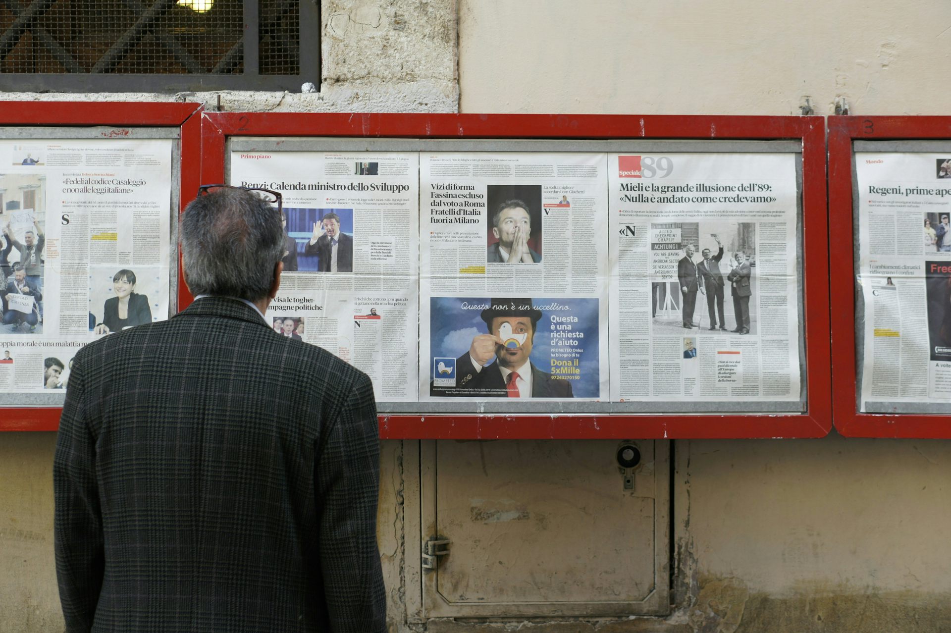 A man reading a newspaper shared publicly behind glass cases.