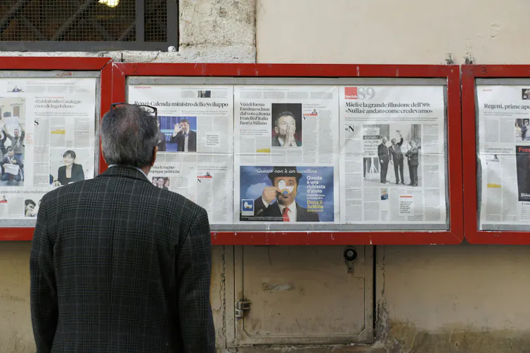 A man reading a newspaper shared publicly behind glass cases.