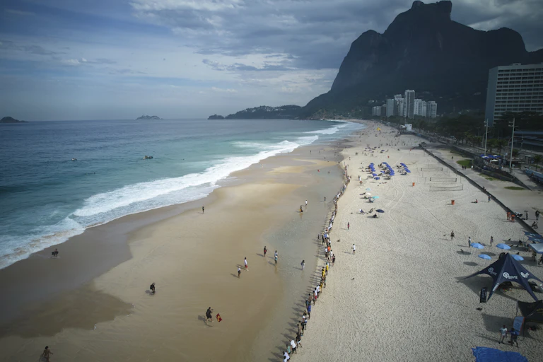 a sandy beach near some tall buildings and a green mountain