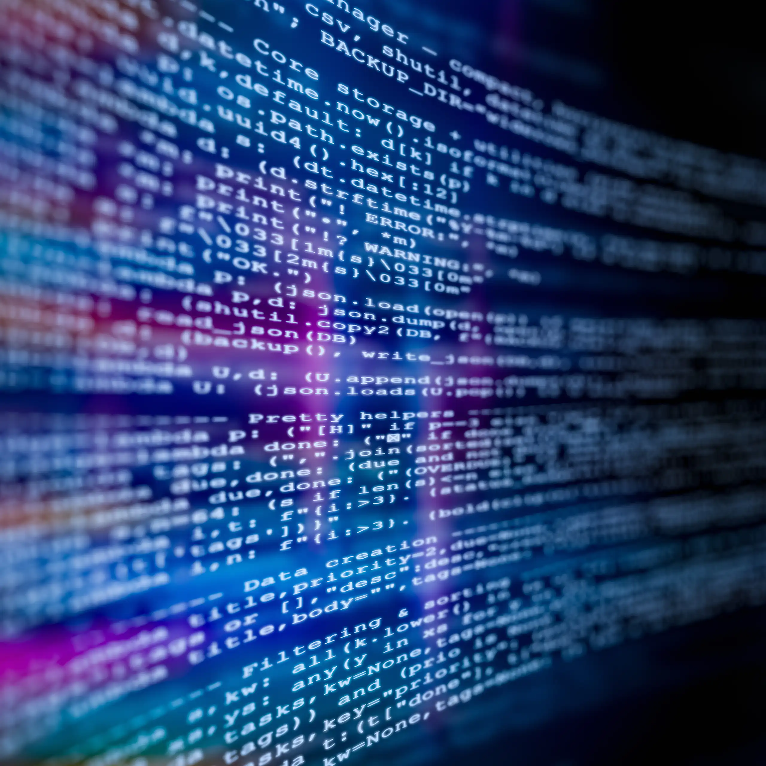Close-up view of computer code displayed on a digital screen, with blurred lines of text and glowing blue and purple light reflections.