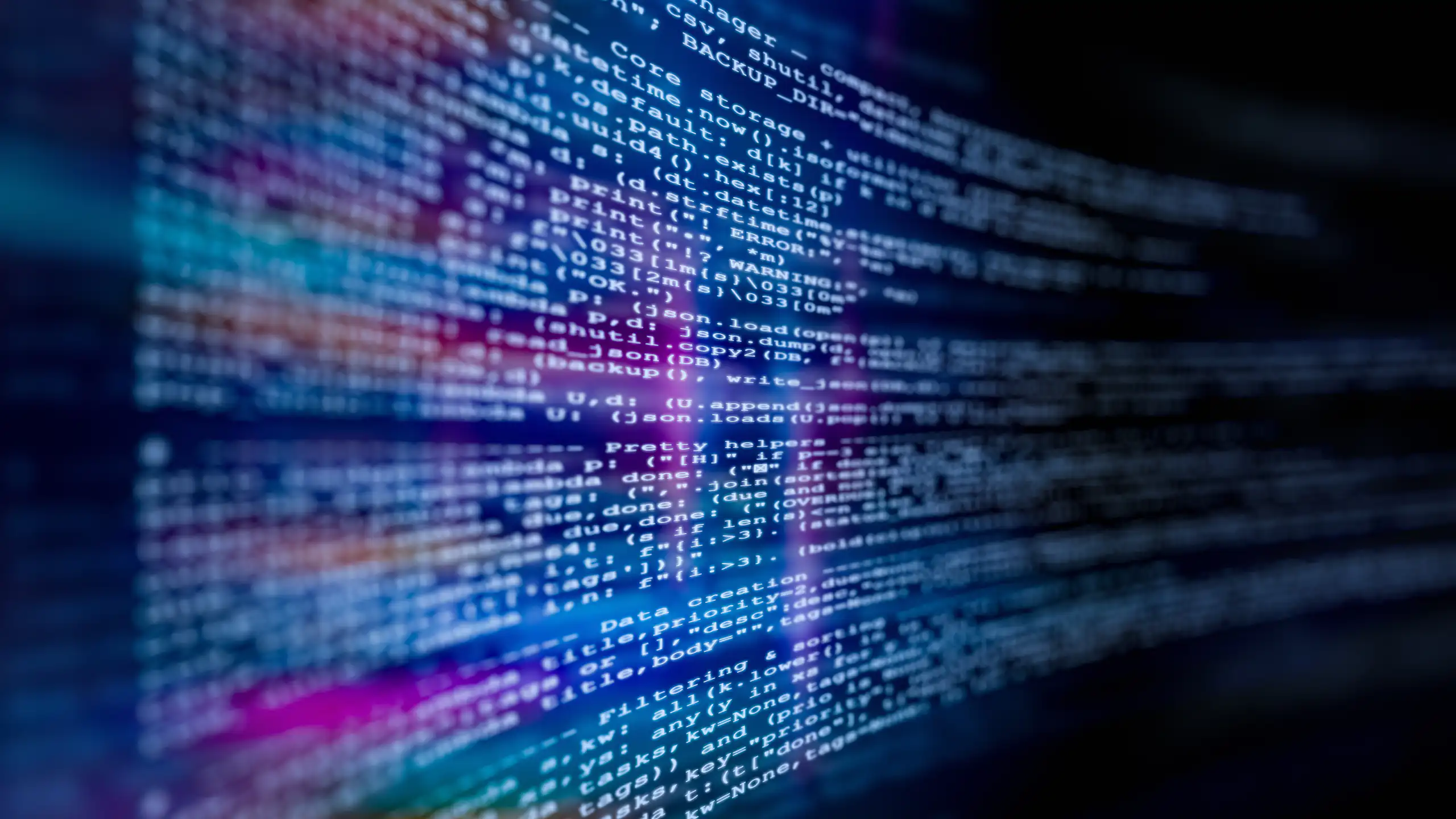 Close-up view of computer code displayed on a digital screen, with blurred lines of text and glowing blue and purple light reflections.