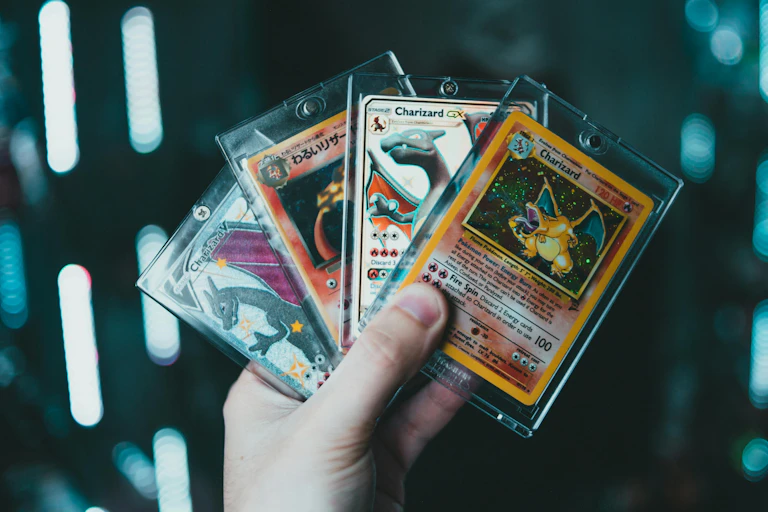 A hand holds four encased Pokemon cards fanned out.