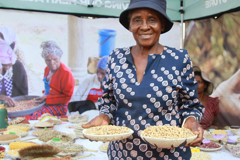 A woman stands at a market holding two big bowls of seeds