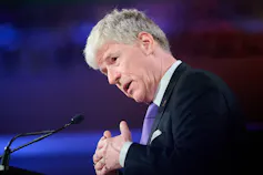 Un hombre de pelo gris habla desde un micrófono.