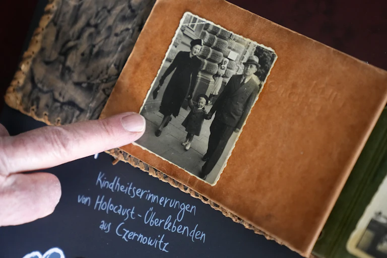 A close-up of a finger pointing at an old photograph of a couple and their child.