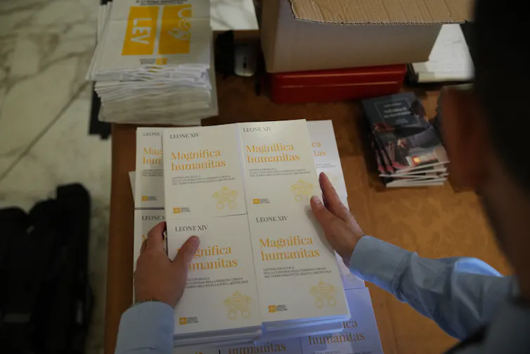 A person holds copies of a document titled Magnifica Humanitas.