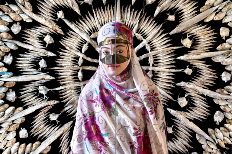 Portrait of a woman wearing a patterned floral headscarf and face covering against a black background. Behind her, small fish are arranged in a symmetrical, radiating pattern.