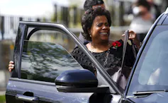 Una mujer negra sonríe mientras sube a su coche.