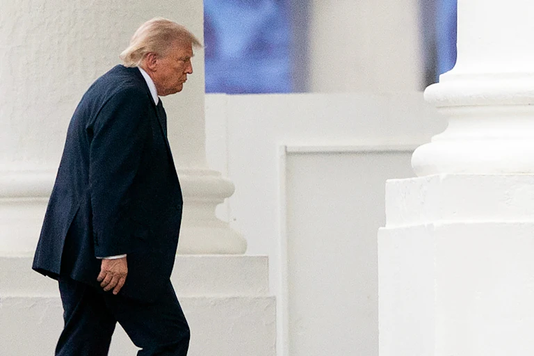 Donald Trump alors qu'il entre dans un bâtiment en pierre blanche.