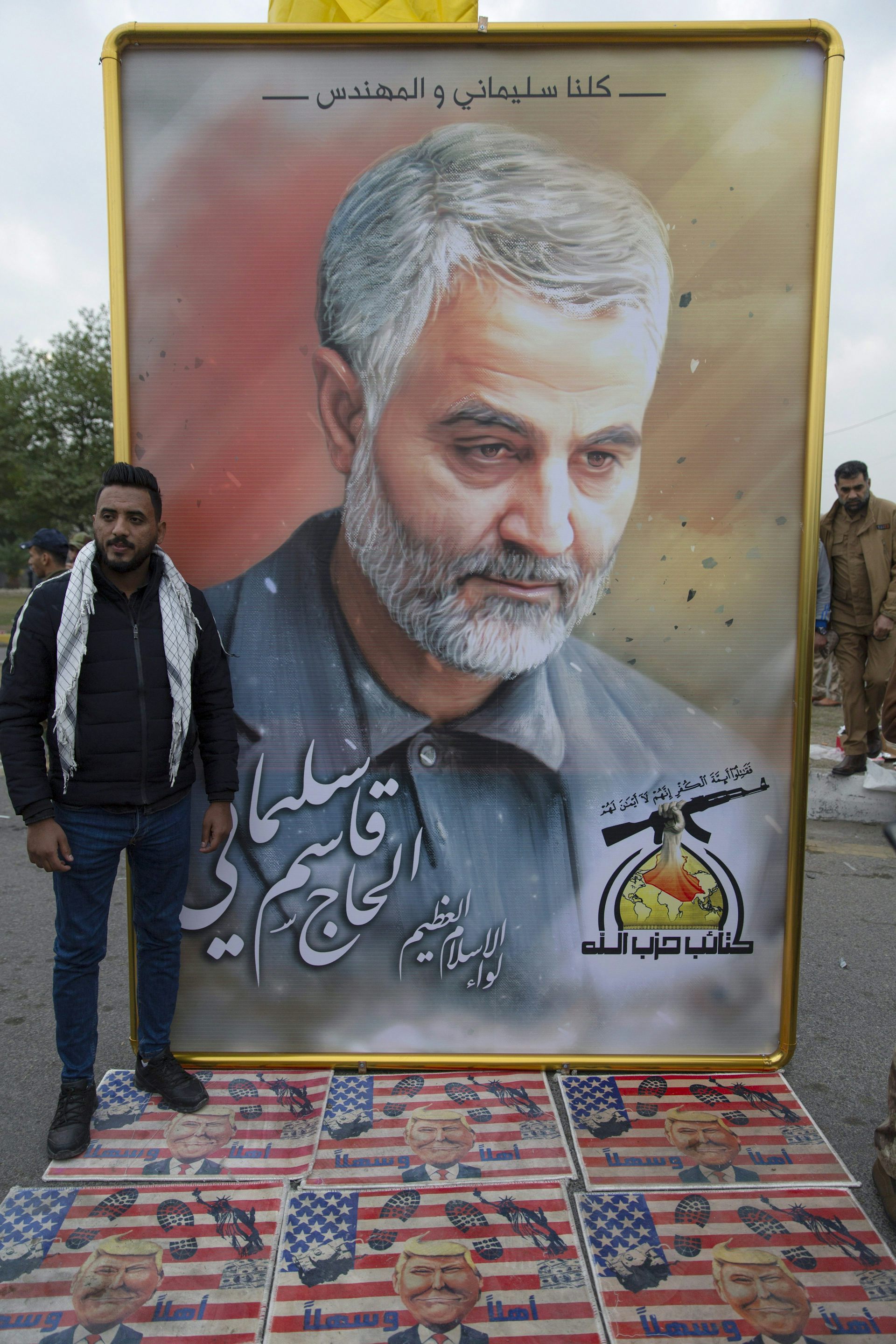 Los dolientes caminan sobre banderas estadounidenses con fotografías del presidente estadounidense Donald Trump debajo de una fotografía de Qassem Soleimani.
