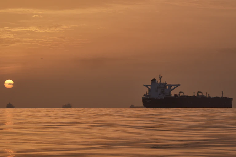 A sun rises behind tankers on the water