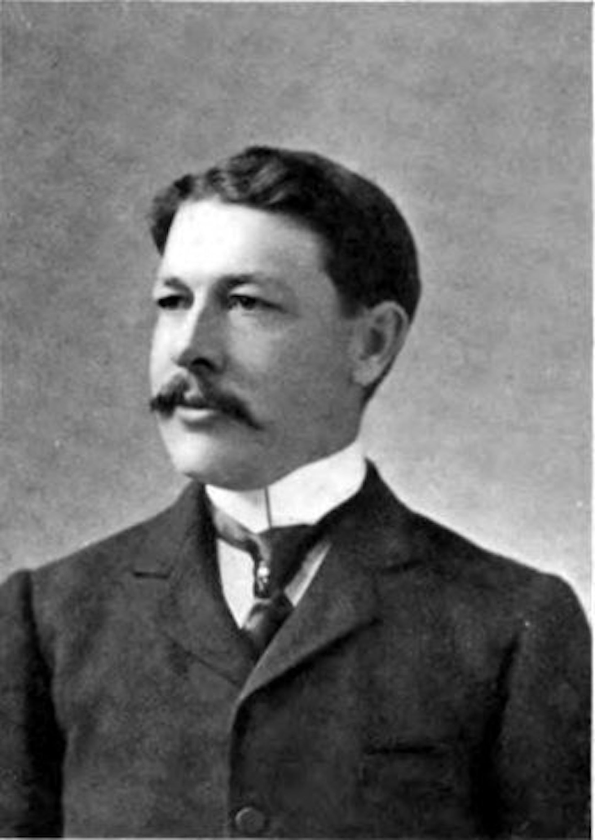Fotografía en blanco y negro de un hombre blanco de mediana edad con bigote y traje.