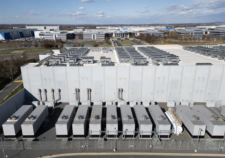 Metal boxes are in a line next to a much larger building.