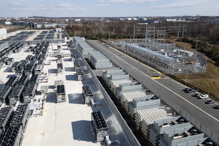 Electrical transmission equipment sits in an area near a large commercial building.