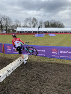La cycliste Rafaelle Carrier enjambe un obstacle en tenant son vélo dans ses mains