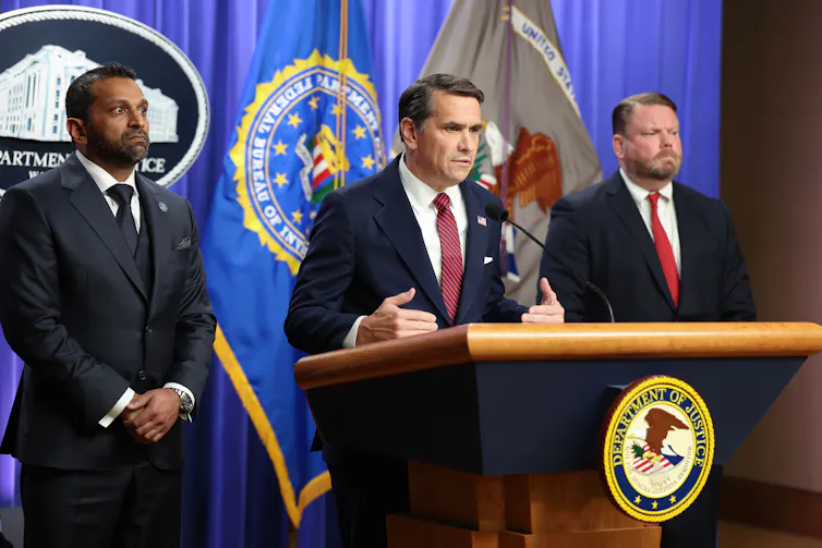 Three men stand behind a lectern as one man speaks.