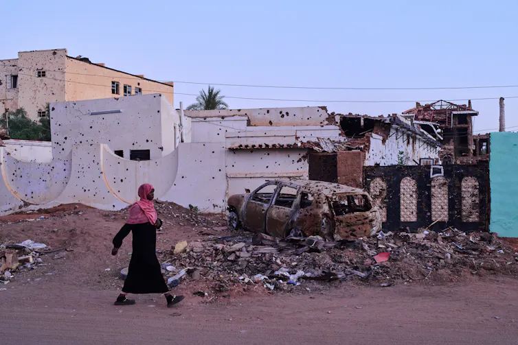 A woman walks along a destroyed street in Sudan.