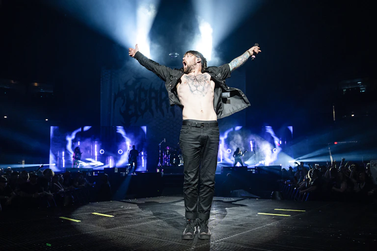 A performer onstage throws his arms out while facing the crowd.