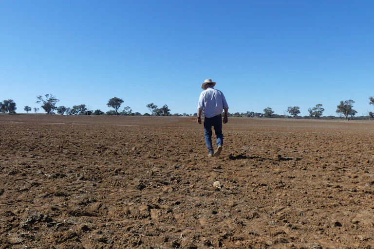 A farmer walks across dry soil.