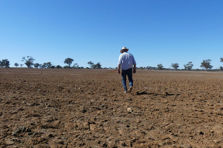 A farmer walks across dry soil.
