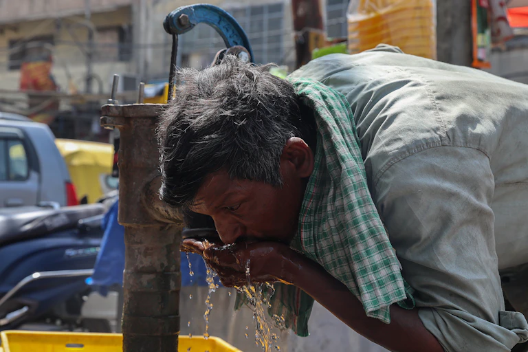 man drinking from water pump in India, heatwave.