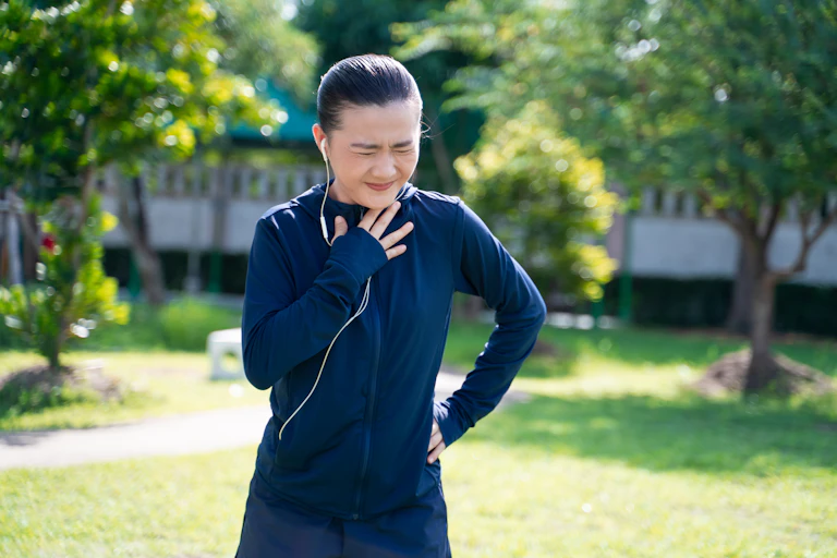 A young woman wearing workout wear holds her chest while she struggles to breathe.