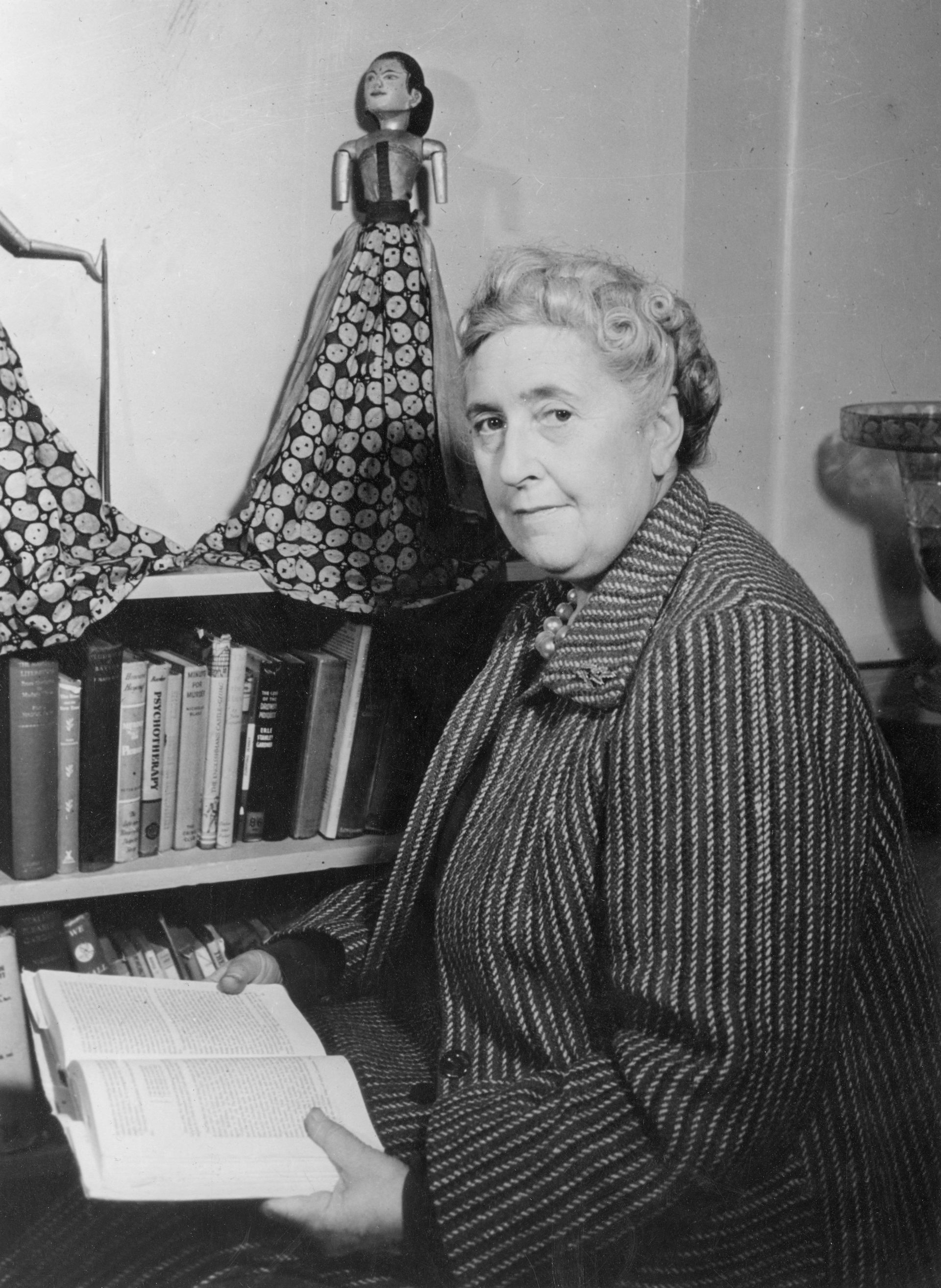 A black and white image of an older woman holding a book looking at the camera.