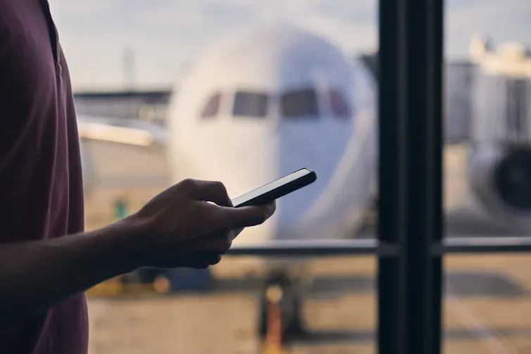 Silhouette of hand of passenger while using mobile phone during waiting in airport terminal.