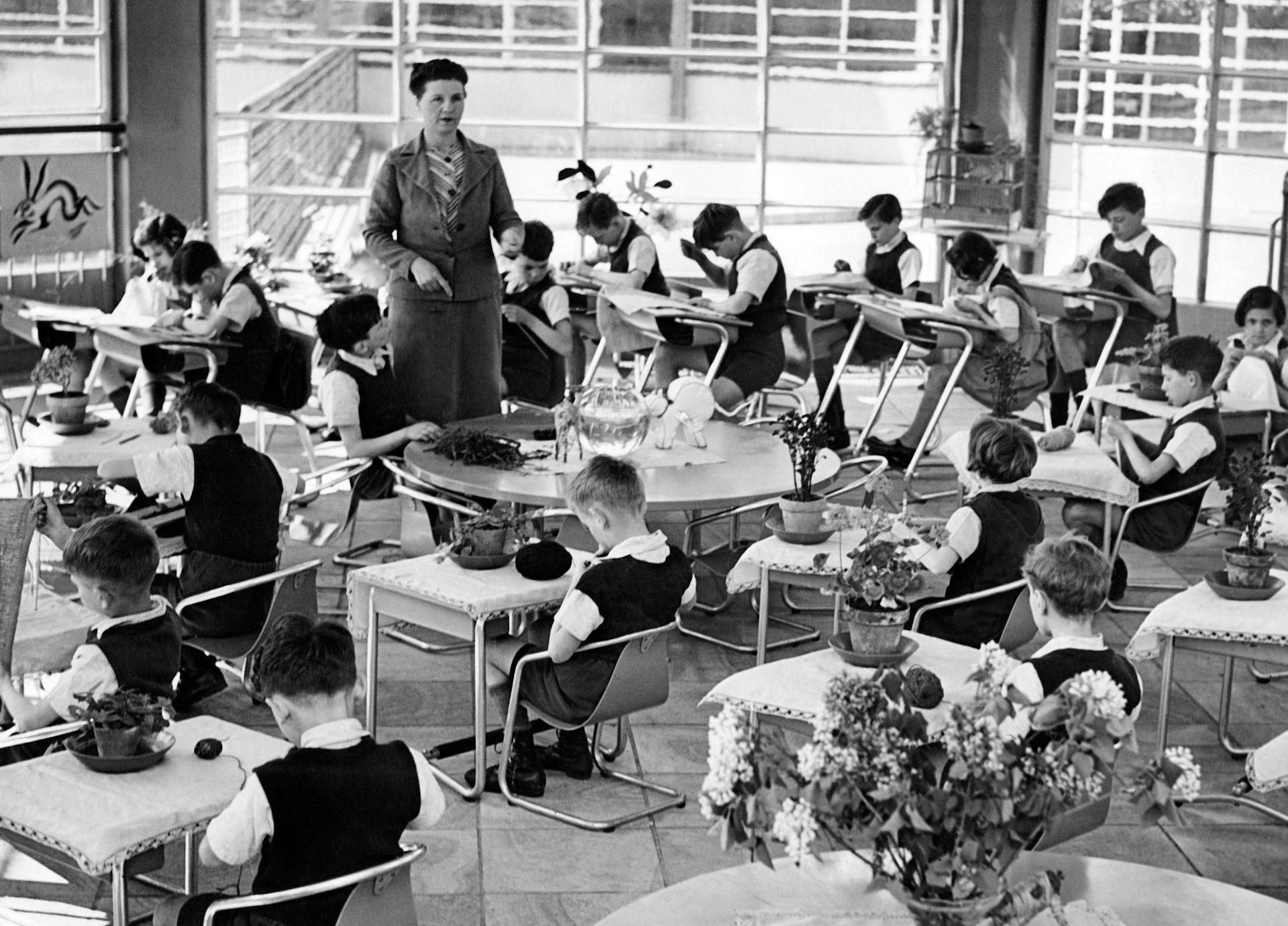 Photo prise en classe : les bureaux des élèves sont disposés en cercle, l'institutrice se tient au centre.