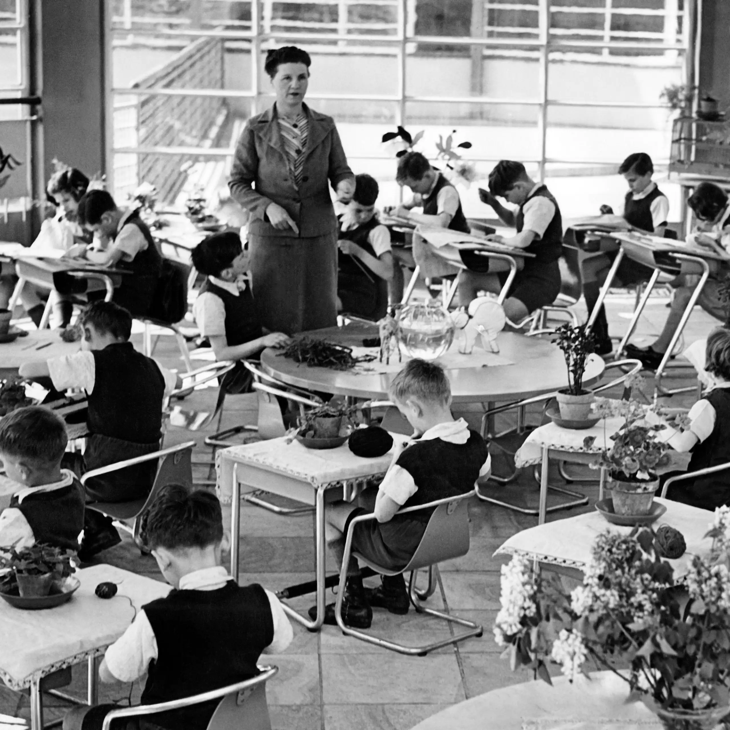 Photo prise en classe : les bureaux des élèves sont disposés en cercle, l'institutrice se tient au centre.