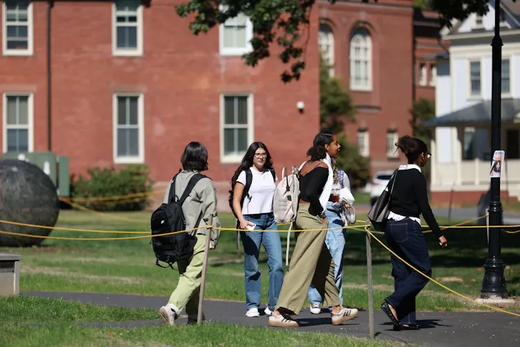 A few young women stand together in front of a red brick building on a green lawn.