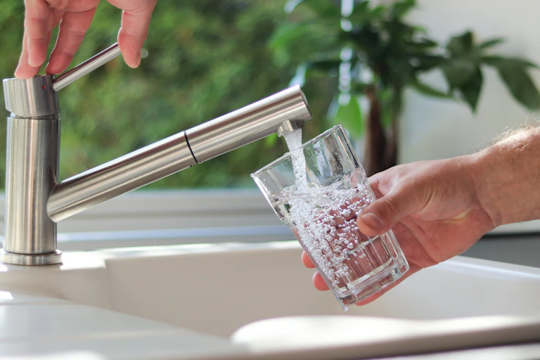 Una mano abre un grifo de cocina mientras otra sujeta un vaso bajo el chorro