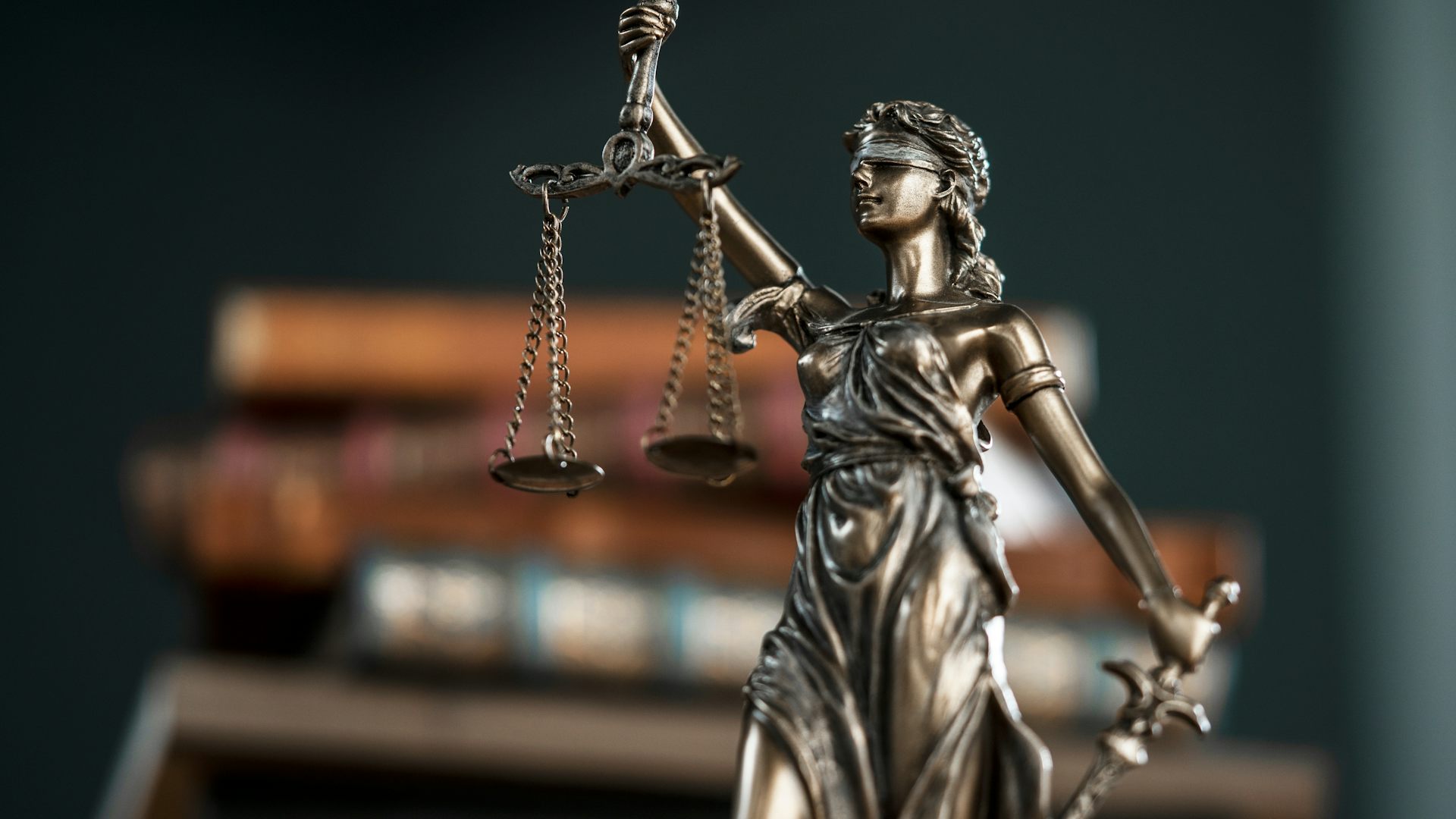 statue of lady justice with scales in front of a stack of books