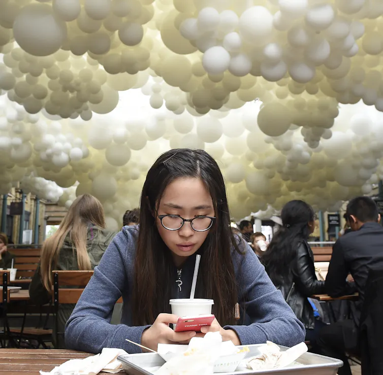Young woman using phone under an art installation in London.