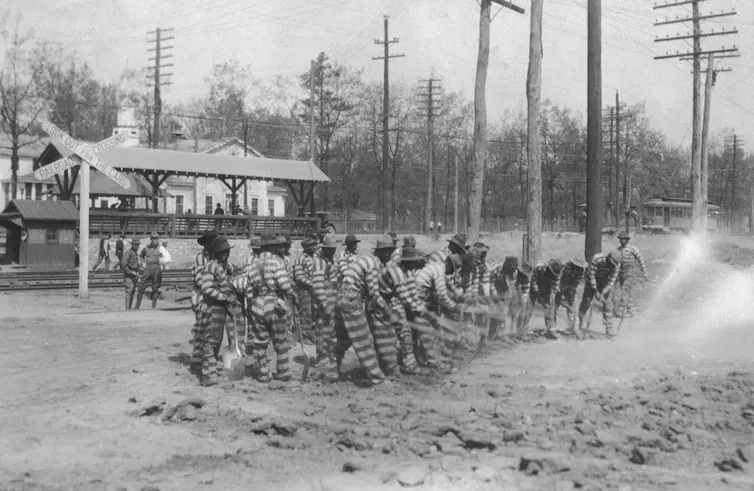 A black-and-white photo of men in striped clothing shoveling the ground.