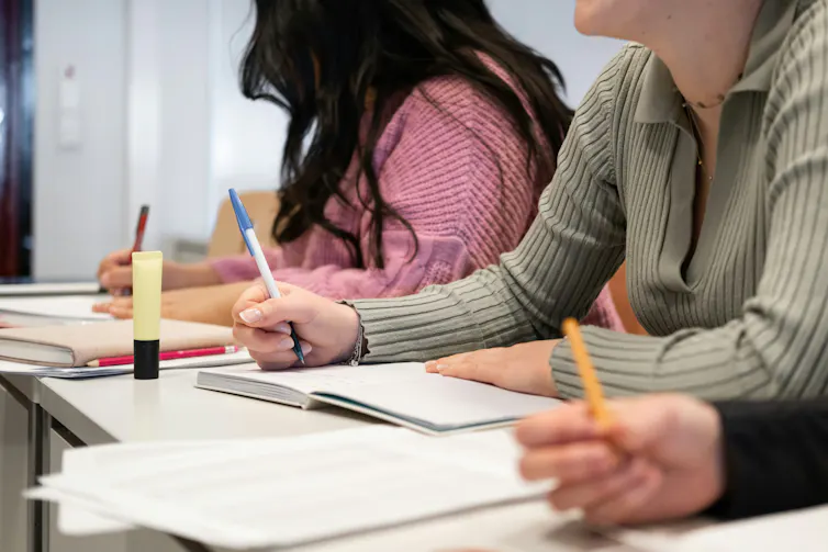 Deux étudiantes dont on ne voit pas les visages écrivent à leur place de travail dans une salle de classe