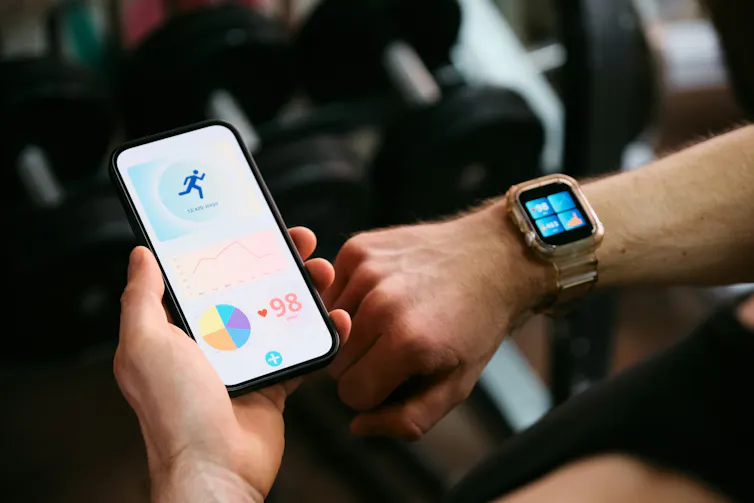 Después de cargar sus datos en la nube, ¿a dónde van? El desafío de las tecnologías de doble uso 1 Primer plano de un hombre sosteniendo un teléfono en la mano izquierda y un reloj inteligente en la muñeca derecha.