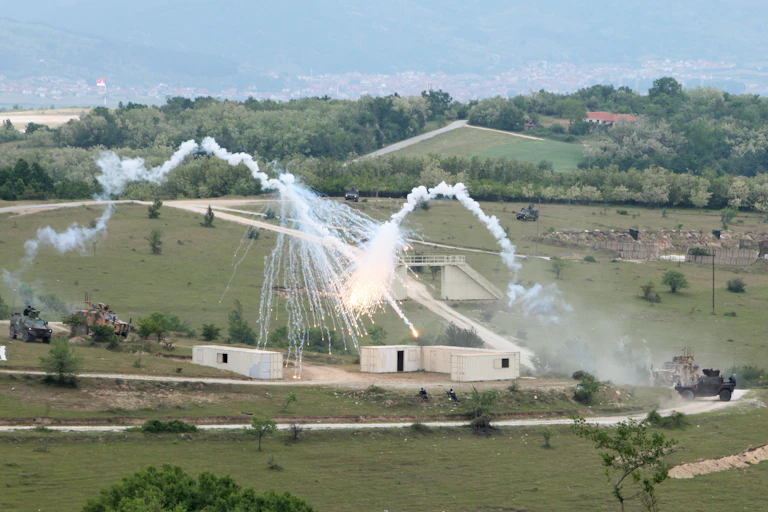 A military exercise featuring smoke and plumes of water in a field.