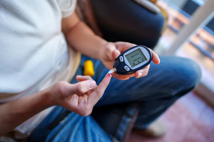 Person pricking finger with blood glucose monitor