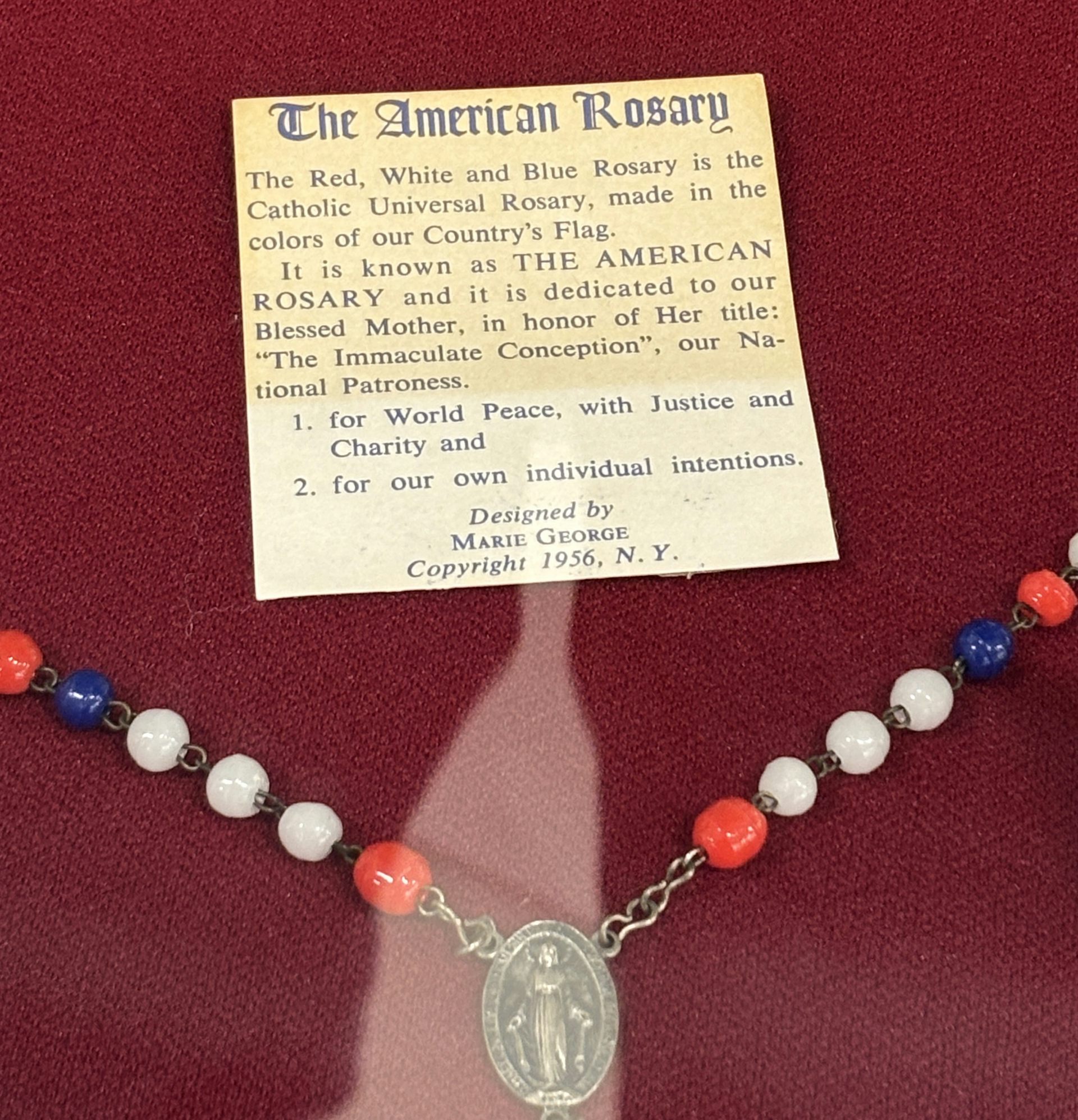 A small explanatory card is positioned next to a string of red, white and blue beads on a chain with a religious medallion.