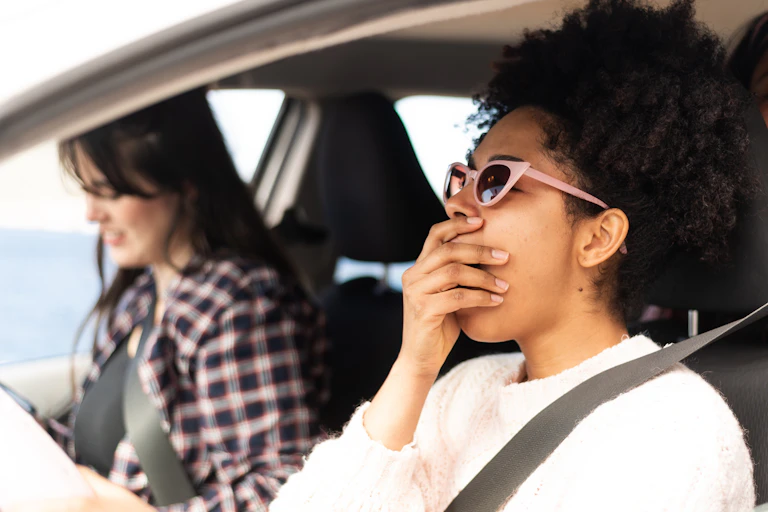 Woman yawning at the wheel of the car while road tripping with a friend.