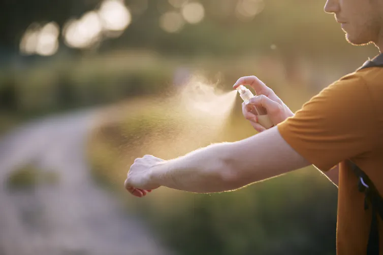 A man spraying his arm with insect repellent outdoors.