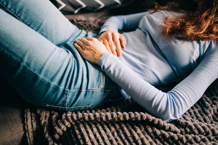 Young woman lying on sofa, hands over stomach