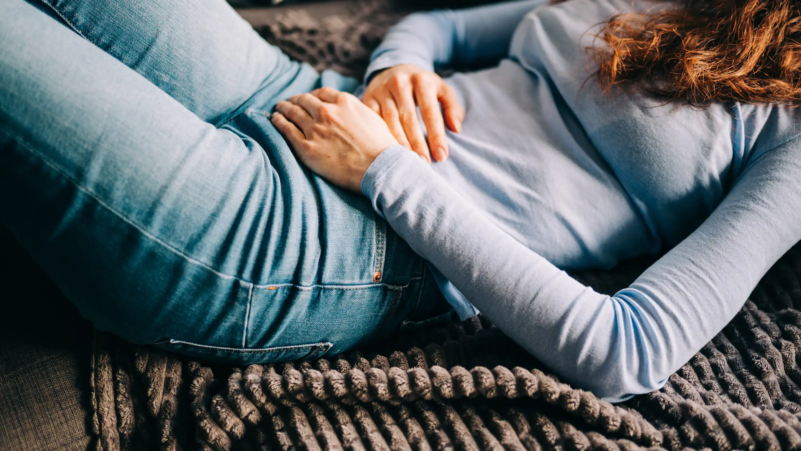 Young woman lying on sofa, hands over stomach
