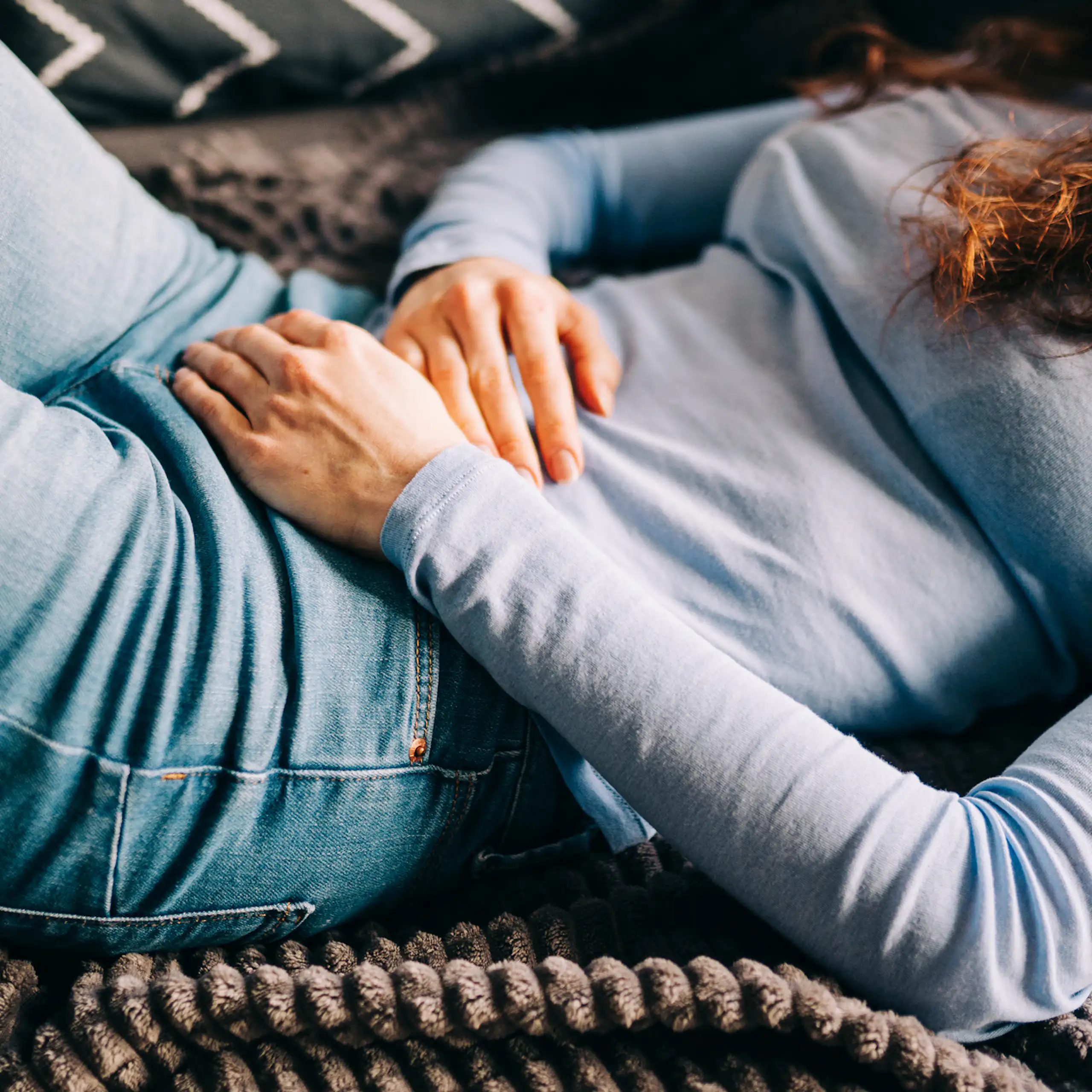 Young woman lying on sofa, hands over stomach