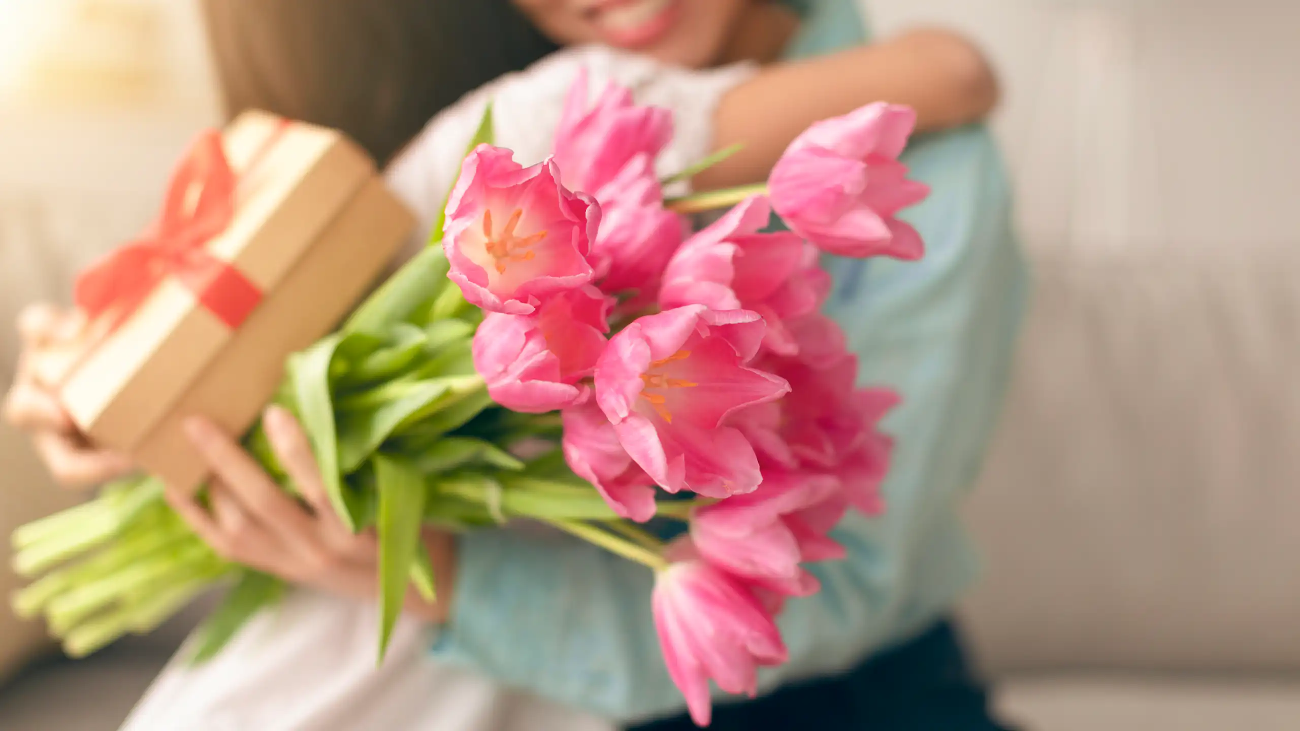 A mother with a bouquet of flowers and a gift hugs her daughter.
