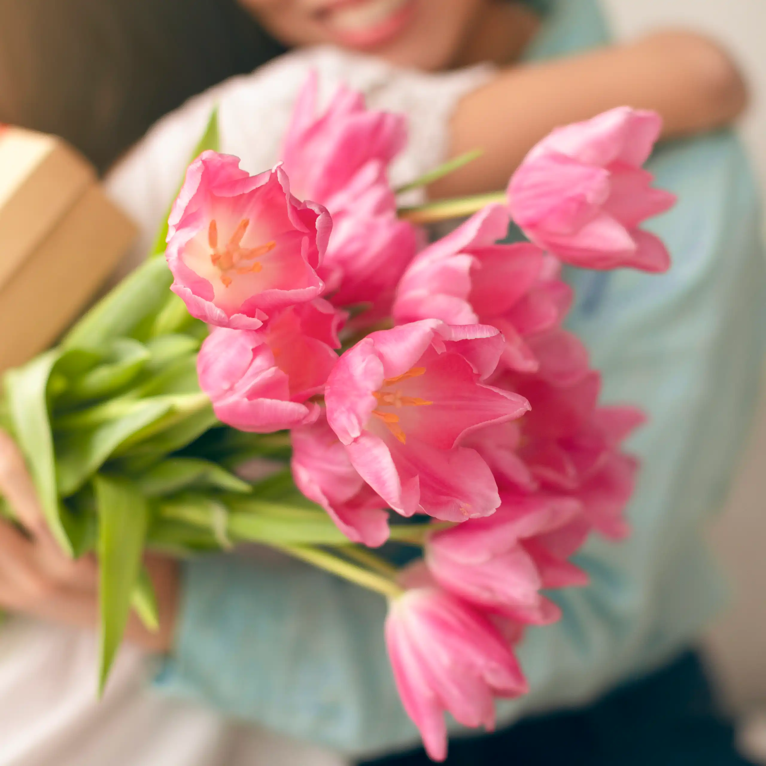 A mother with a bouquet of flowers and a gift hugs her daughter.